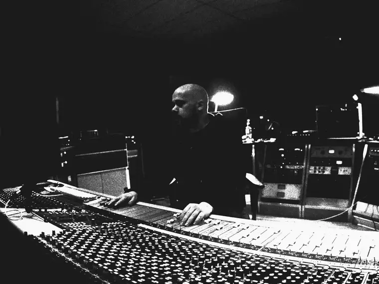 Someone at a large analogue console in a dark control room, hands on the faders, racks of outboard gear behind.