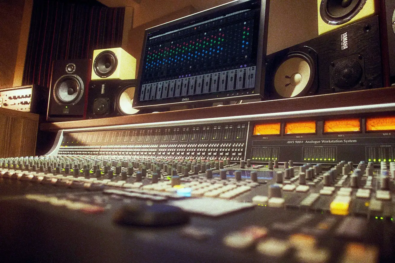 A studio seen from the edge of a large analogue console, with Stereosonic MIX on a screen between the monitors.