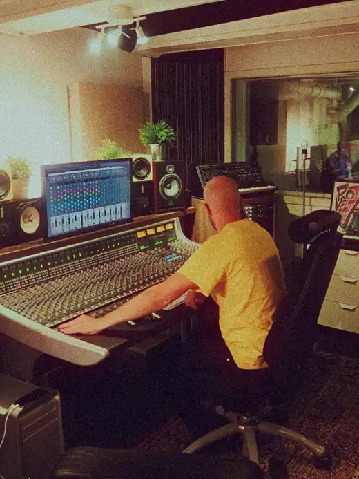 Someone mixing at a large analogue console, with Stereosonic MIX on the screen above it.